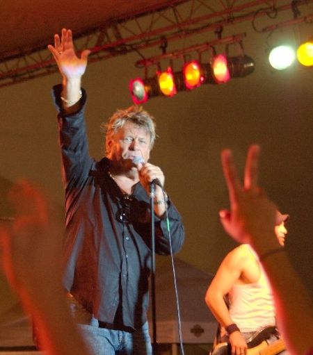 Brian Howe singing at a concert in a black shirt.